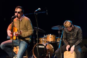 Two men are playing guitar and drums on stage.