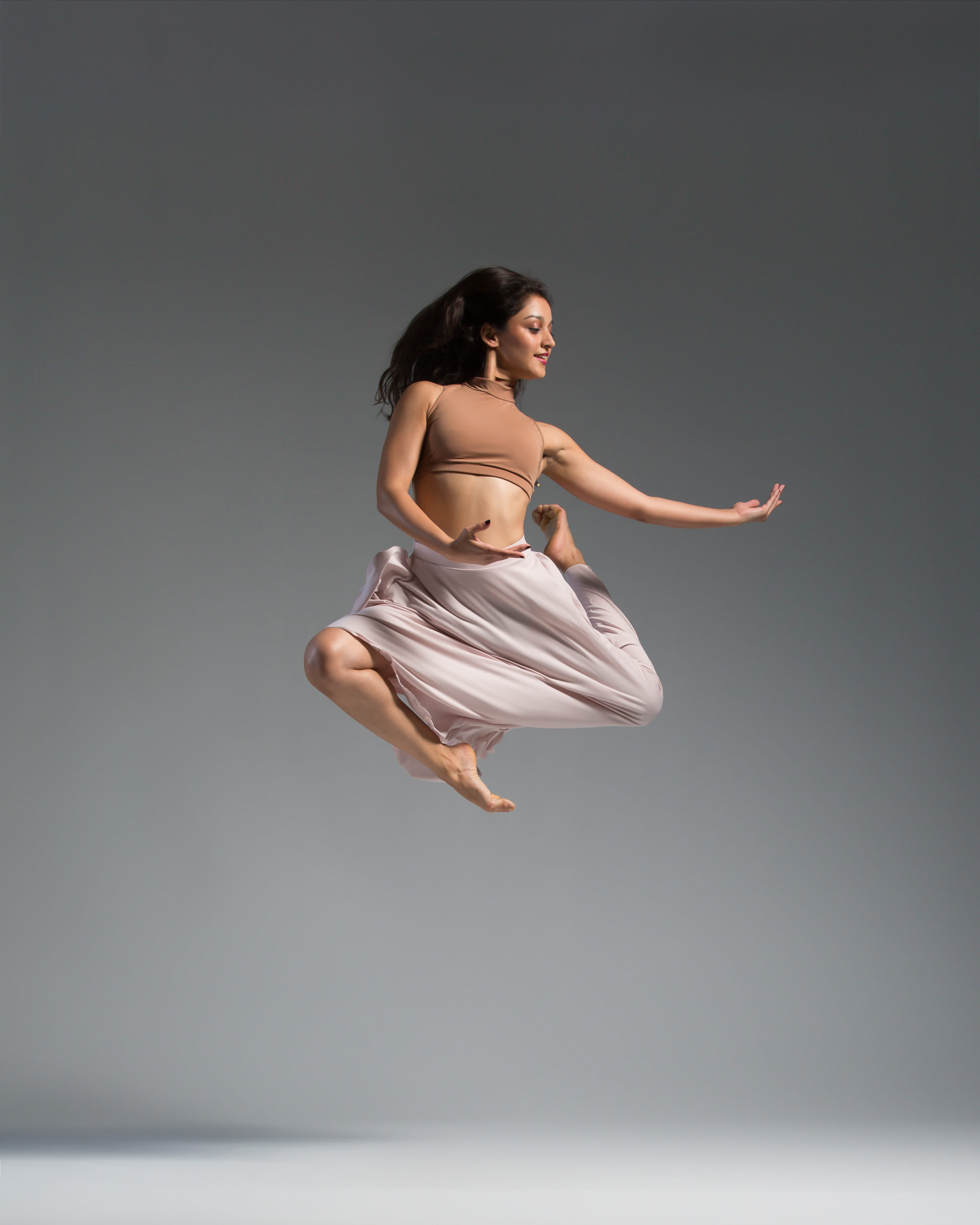 A woman in white leotard jumping up into the air.