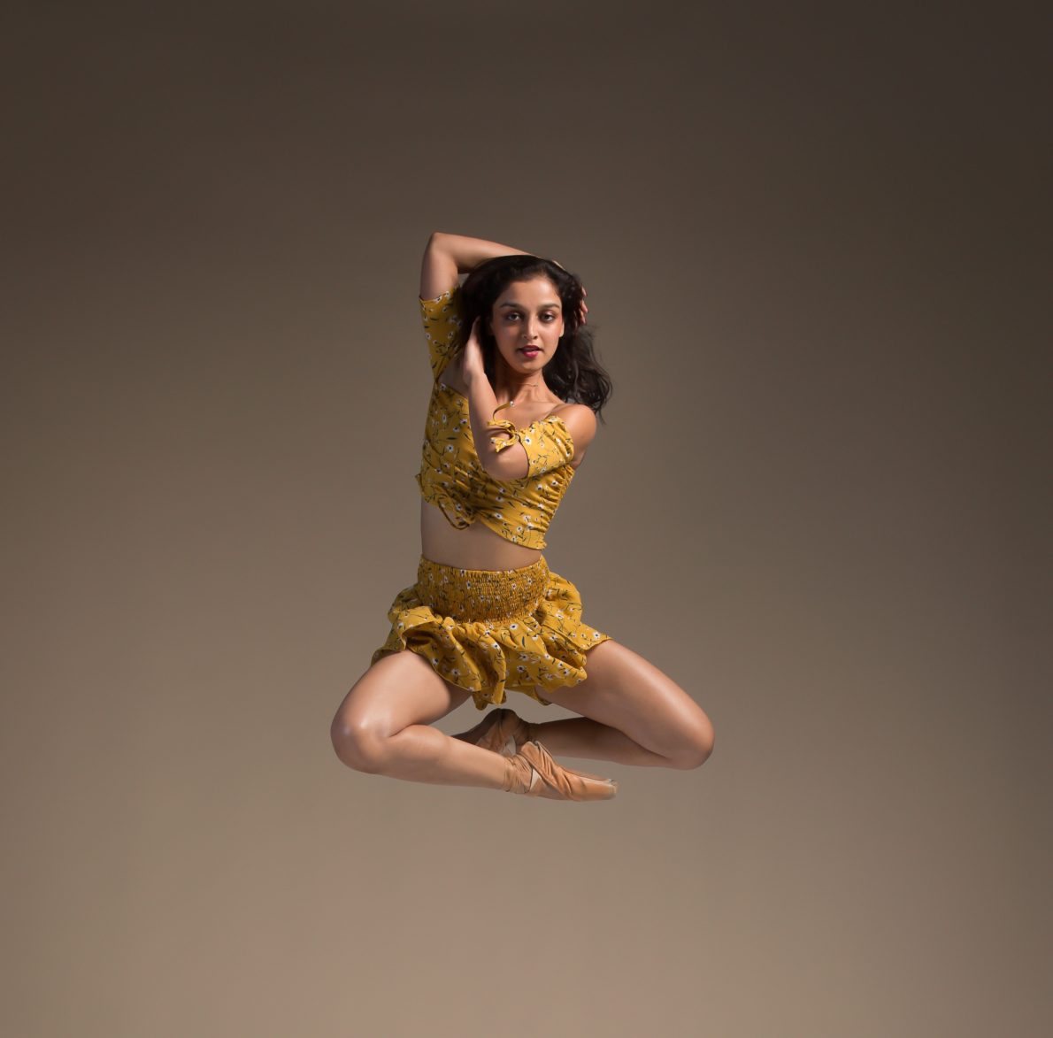 A woman in yellow leotard and skirt jumping.