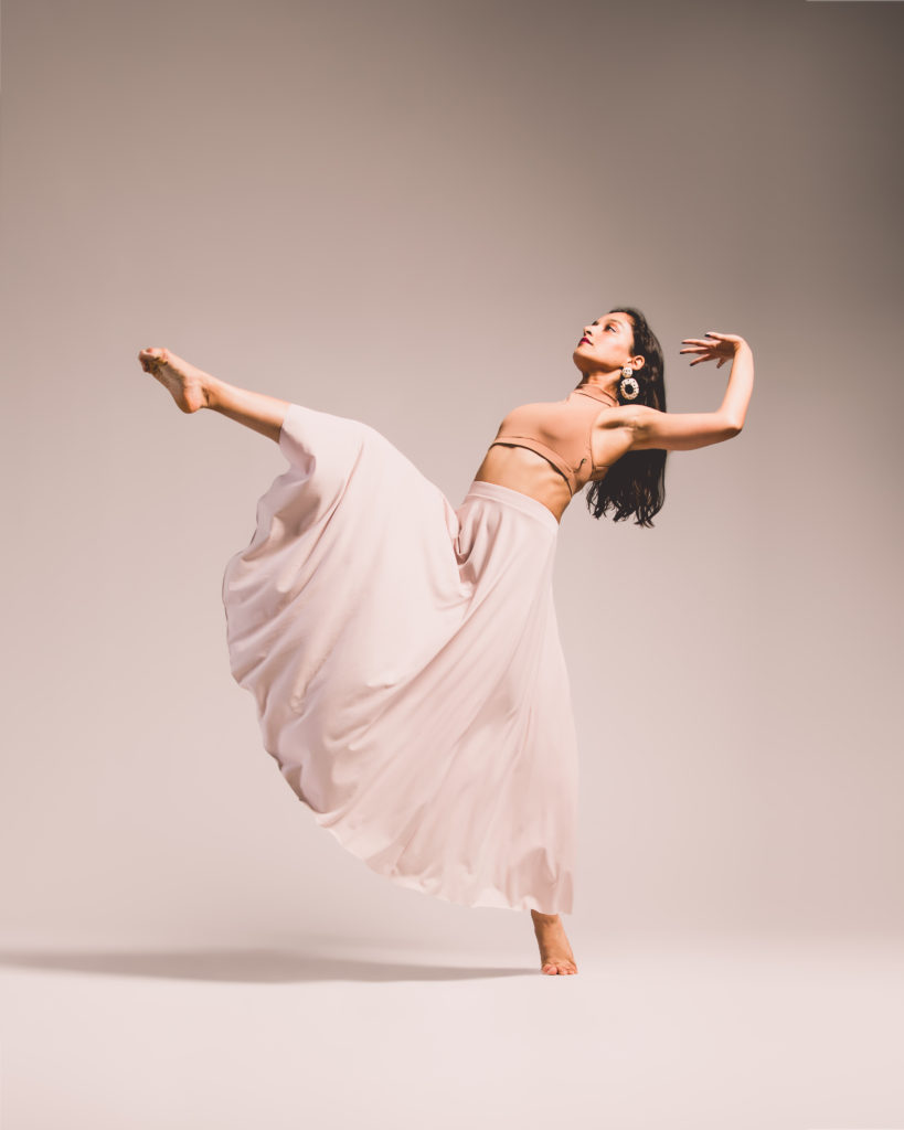 A woman in a rosé skirt dancing on top of her foot.