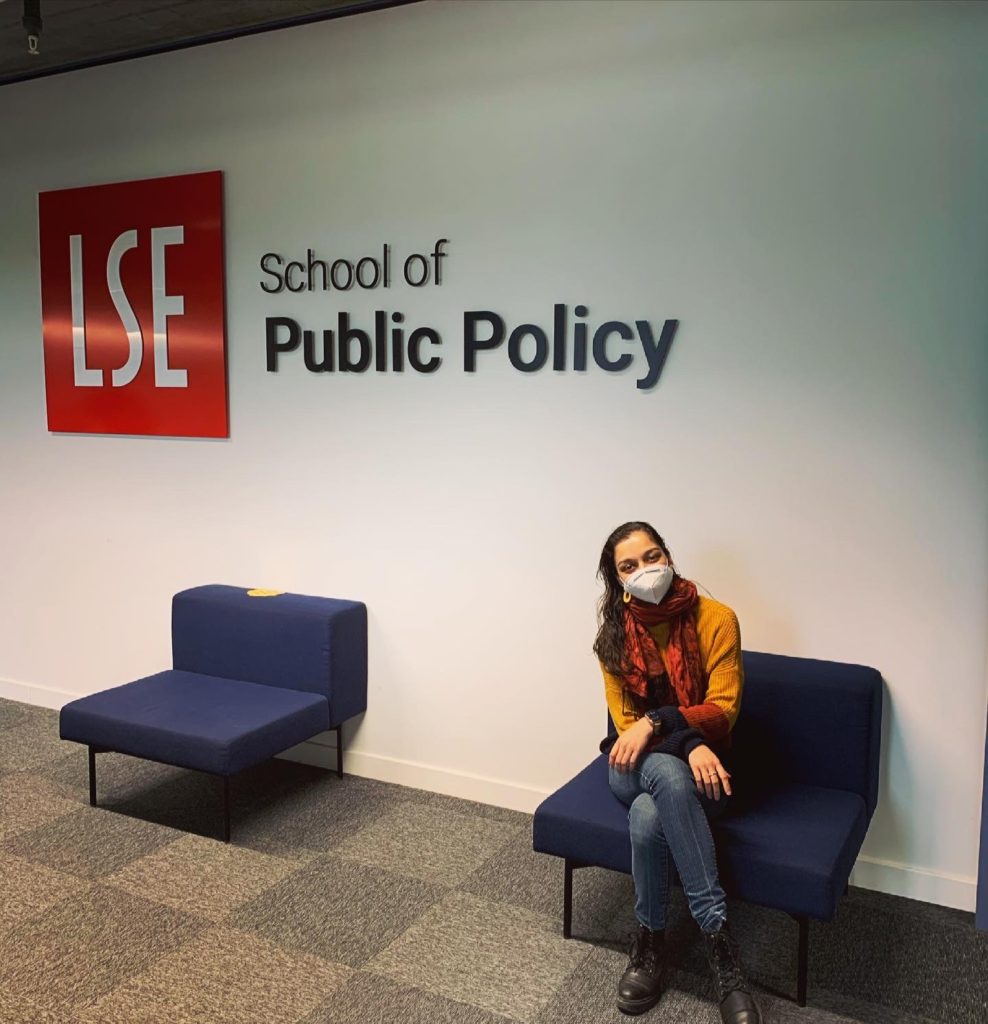 A woman sitting on a blue chair in front of LSE sign.