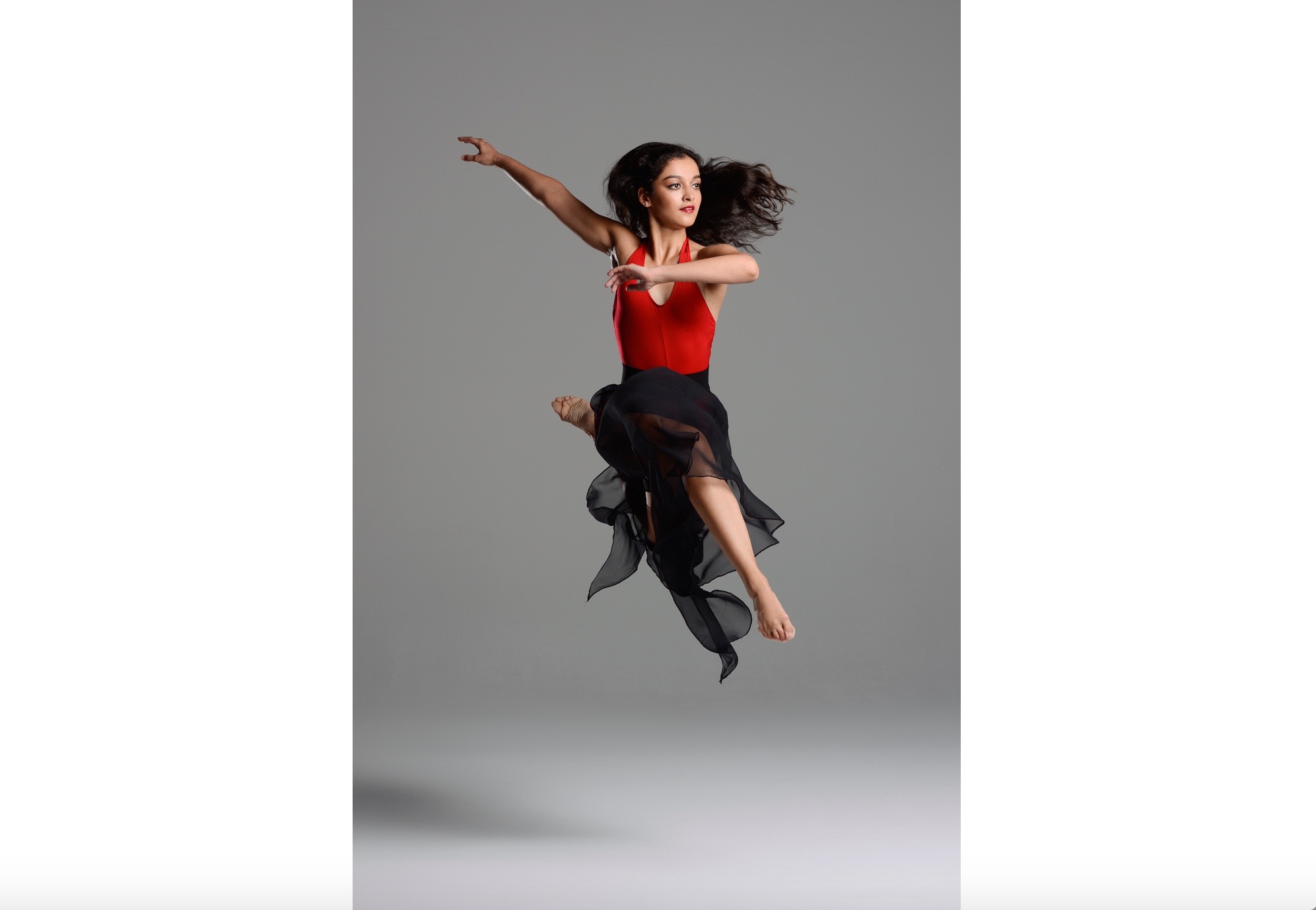 A woman in red shirt and black skirt jumping.